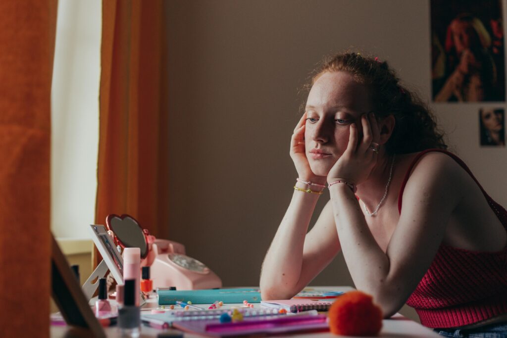 Woman sitting thoughtfully at a desk with vintage items in a cozy room.